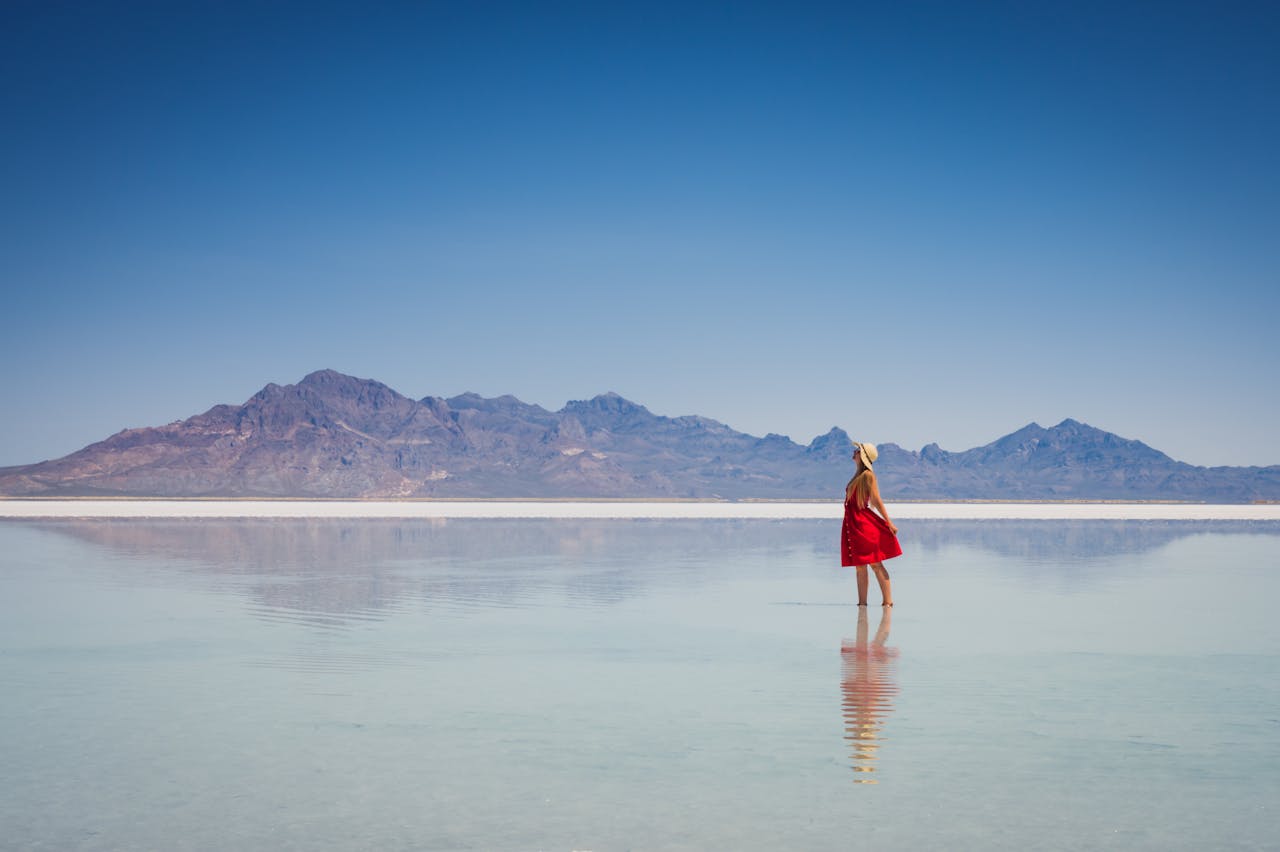 who-we-are A woman in a red dress stands at Bonneville Salt Flats with a view of distant mountains.
